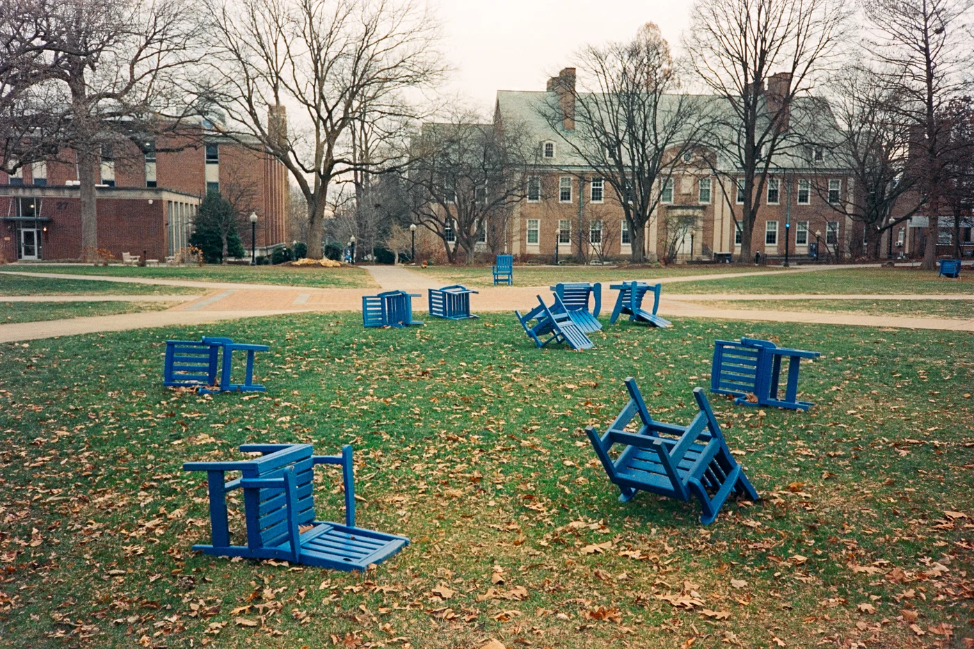 Blue chairs are all strewn about an open college campus lawn.